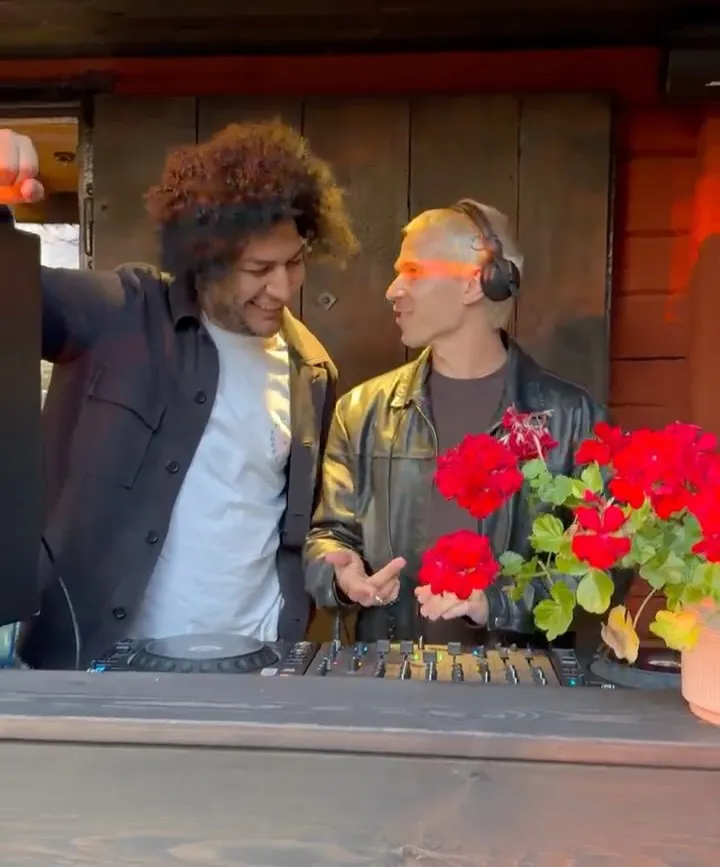 Dos personas pinchando música junto a unas flores rojas.