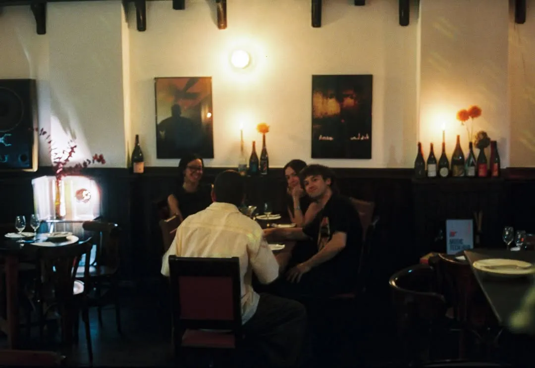 La sala de Bar Manifest de noche: mesas con velas, cuadros en la pared y botellas sobre el friso de madera.