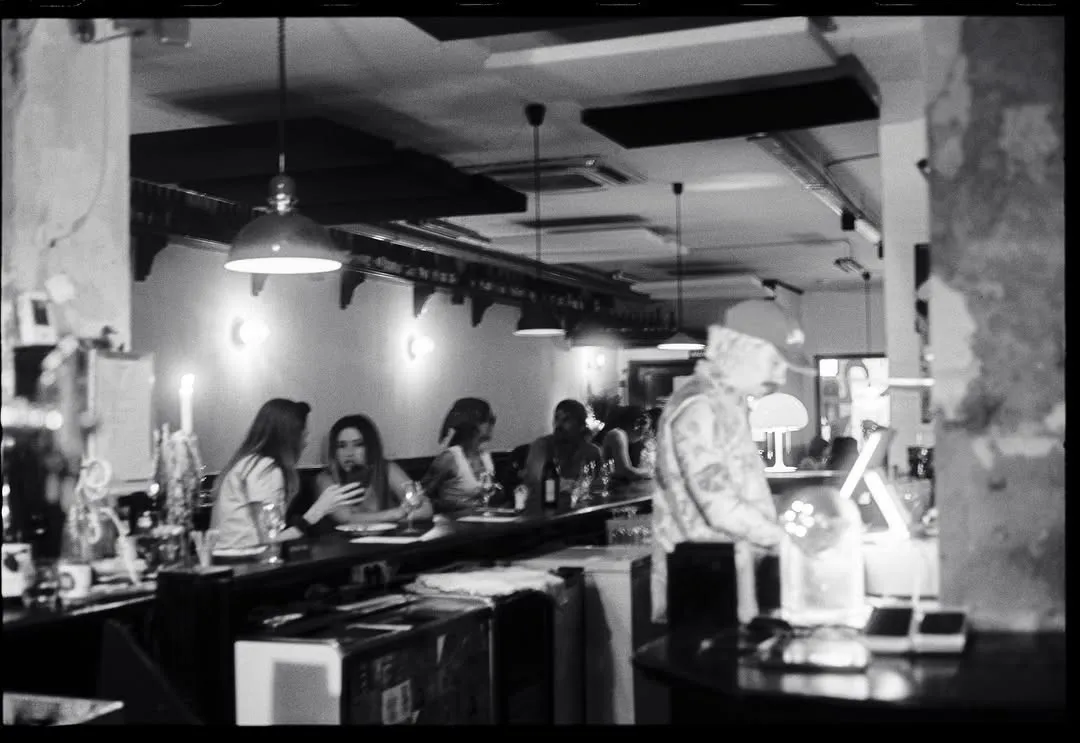 La barra en blanco y negro, con clientes y lámparas colgantes.