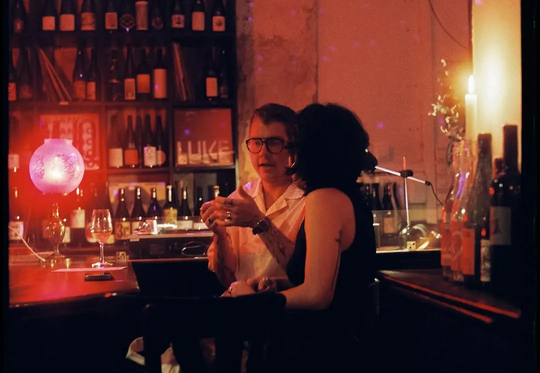 Dos clientes en la barra a la luz de las velas, con botellas al fondo.