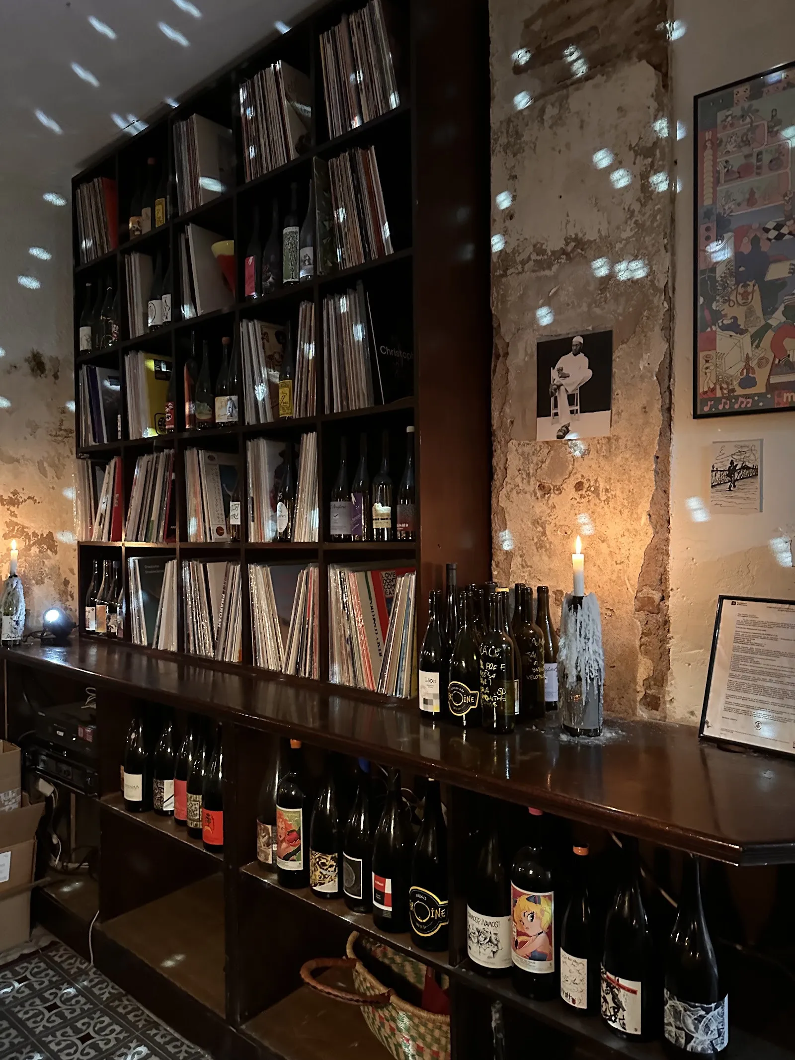La pared de vinilos del bar, con botellas debajo y una vela encendida.