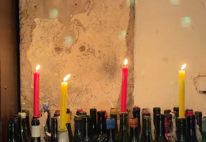 Velas rojas y amarillas encendidas entre botellas vacías.